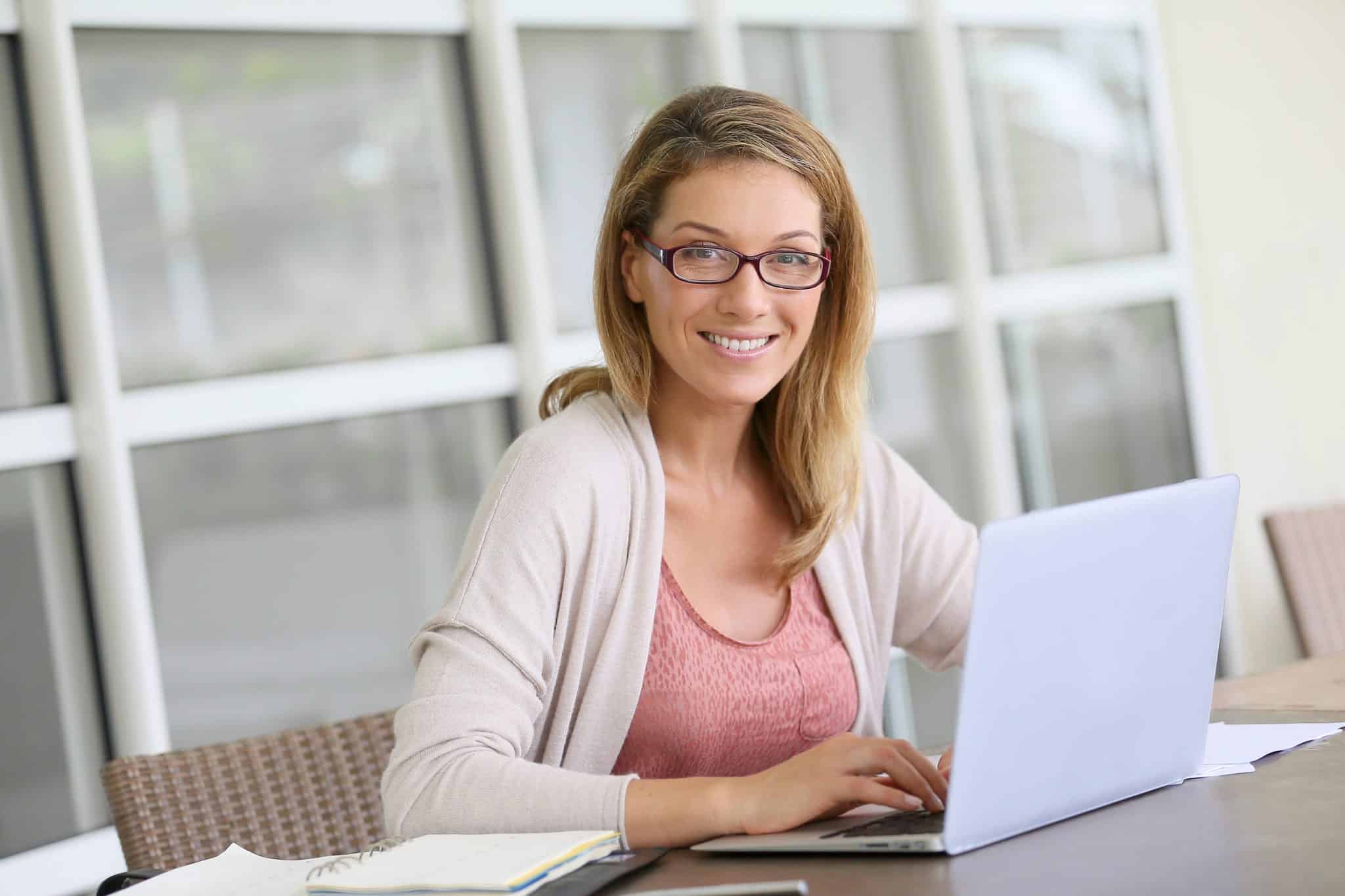 Young woman in glasses poses in front of laptop